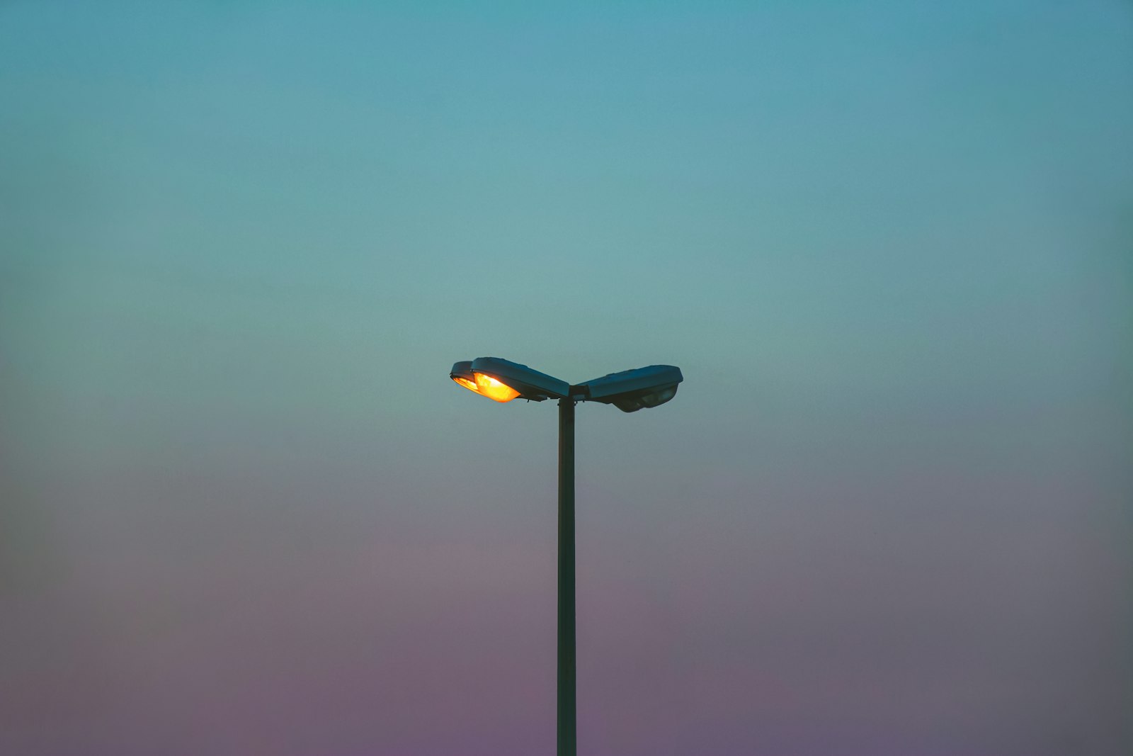 Silhouette of a dual-head streetlight against a dusk gradient sky